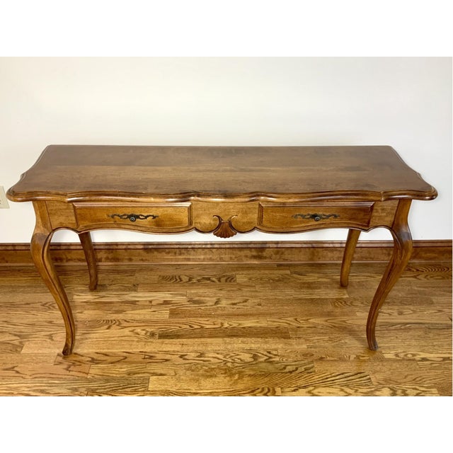 A French Provincial style console sofa table in a warm honey-brown tone with a shaped serpentine top edge, two drawers,...
