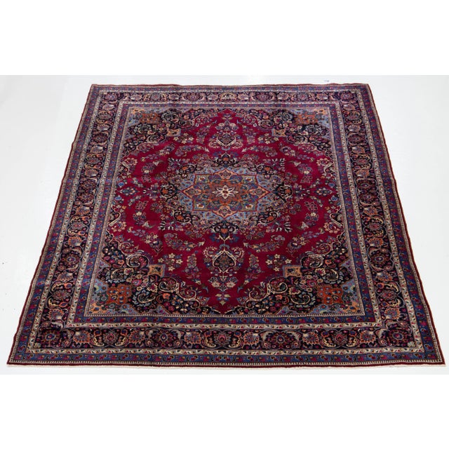 This vintage Persian Kashan hand-knotted wool rug features a red field adorned with a beautiful multicolor rosette design....
