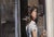 The painting depicts a figure poised at the threshold of an exit, bathed in the interplay of light and shadow that creates...