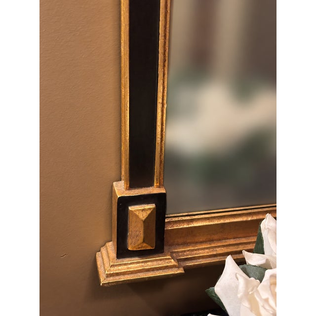 An elegant statement mirror featuring an intricate gold-tone frame with contrasting black accents. The sculptural...