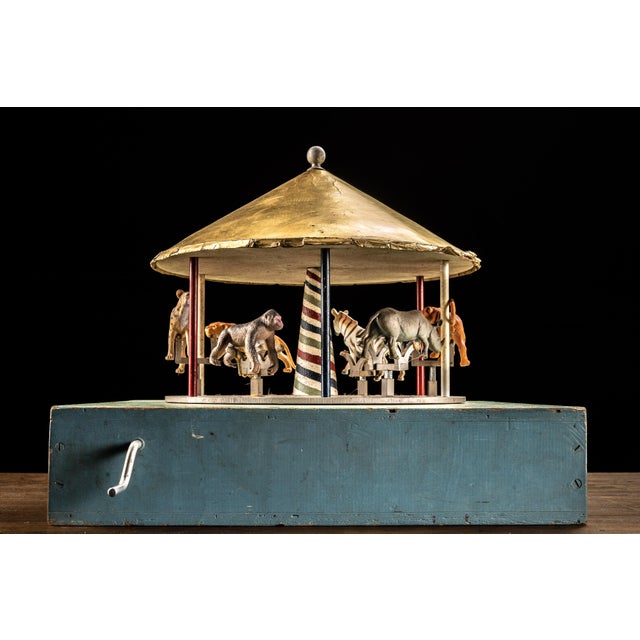 Antique hand-crank mechanical carousel toy featuring an early 20th-century carousel structure mounted on a large painted...