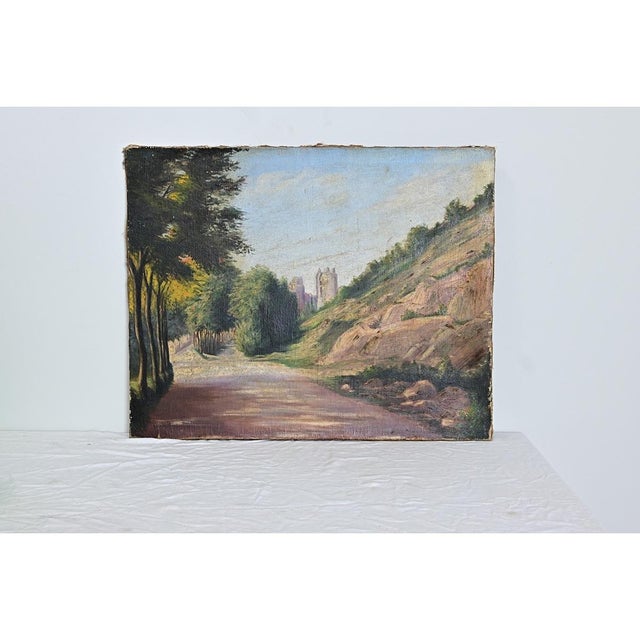 This French early 20th century oil on linen painting illustrates a rustic landscape with a dirt road in the foreground...