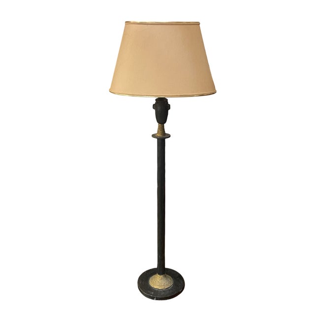 Table lamp with a long, slender body in black. It features a tribal-inspired design, evoking a stylized figure with...