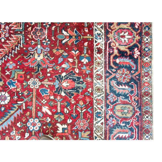 This antique Persian Heriz rug, dating to the 1920s, features a bold geometric design with a prominent central medallion....