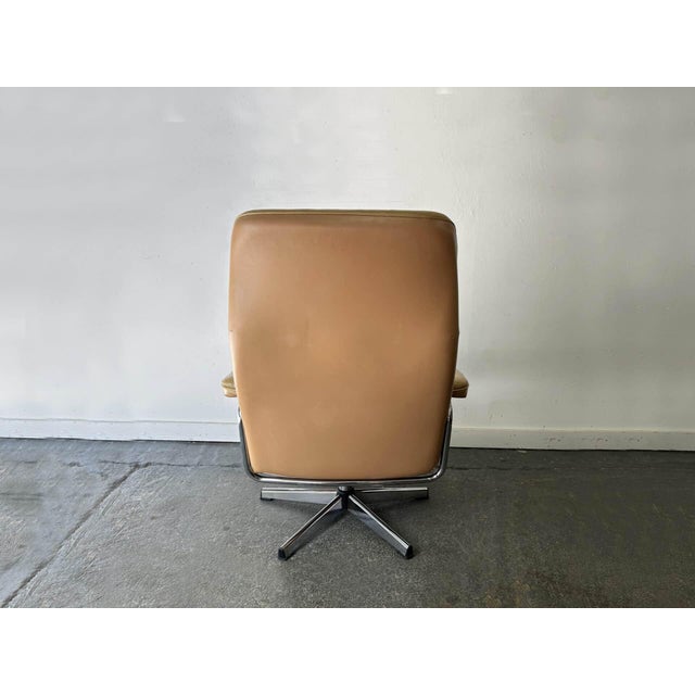 A distinctive 1970s swivel reclining armchair, upholstered in the original tan leather on a polished chrome tubular frame...