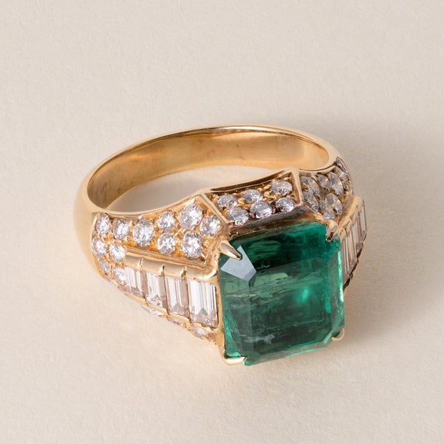 This is a vintage emerald ring featuring a vivid Zambian emerald, accented by baguette and round brilliant diamonds, all...