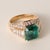 This is a vintage emerald ring featuring a vivid Zambian emerald, accented by baguette and round brilliant diamonds, all...
