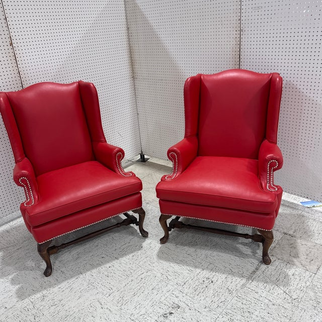 Striking pair of vintage red leather wingback lounge chairs featuring generously padded seats, high supportive backs,...