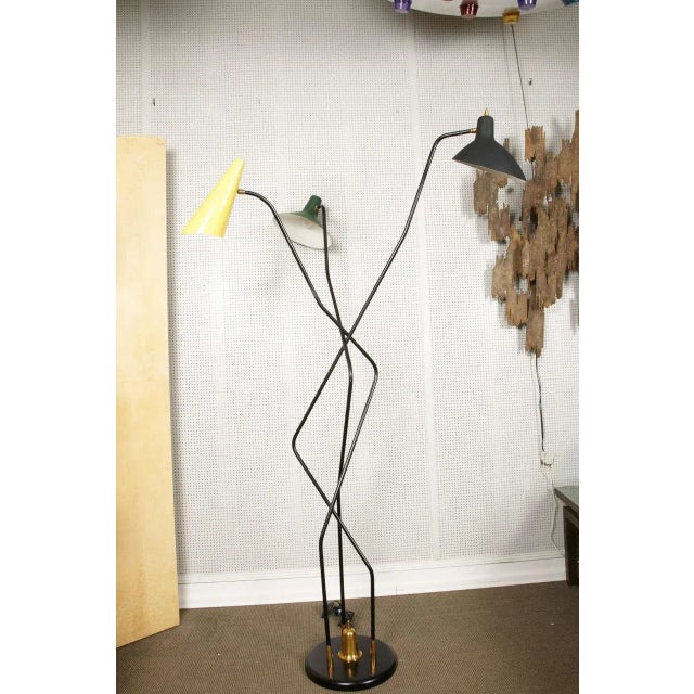 This triennial floor lamp in the style of Stilnovo is made of iron and brass. Up to 250V (Europe/UK Standard).The wiring...