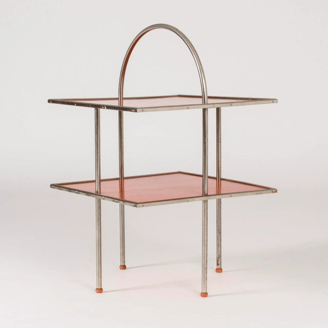 This Swedish functionalist side table features light graphic lines and is made from metal and red-lacquered wood. The...