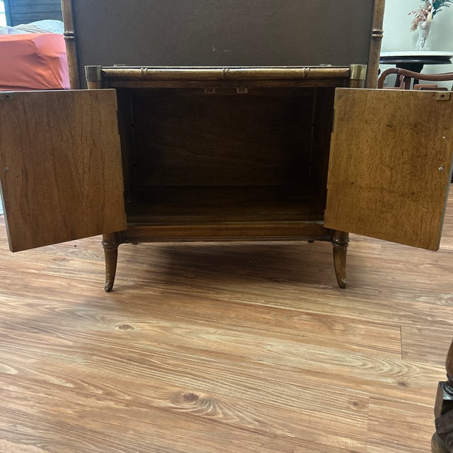 A faux bamboo nightstand by Stanley Furniture, circa 1970s. Two cabinet doors fronted in woven cane with Greek key...