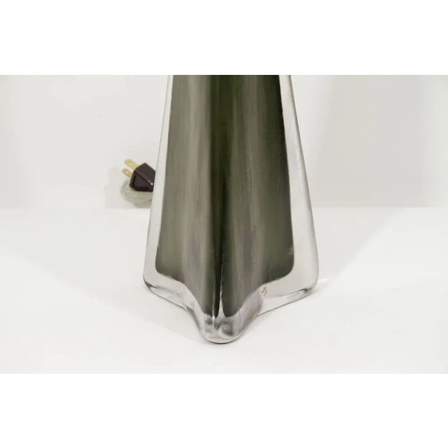 A Carl Fagerlund, Orrefors green table lamp model RD 1319. A triangular formed bottle green glass lamp is encased in a...
