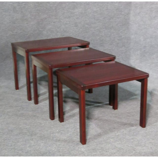 Showing off a deep shade of red rosewood grain, this vintage set of nesting tables is unique and full of Mid-Century...