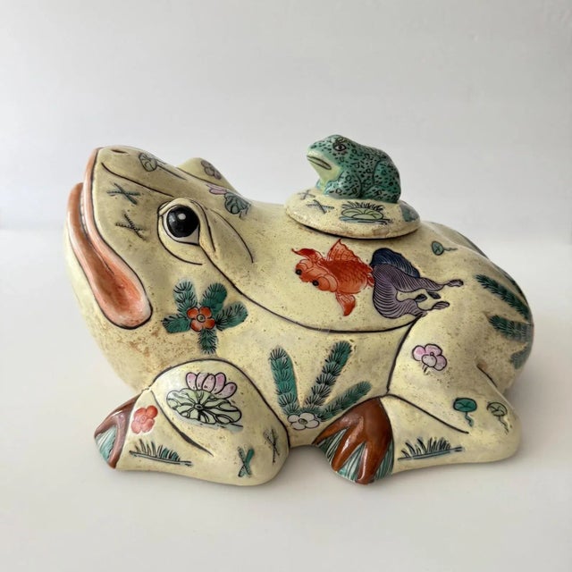 Charming frog with a toothy smile and a smaller frog (lid) on its back. Decorated with fish and flowers and with a Chinese...