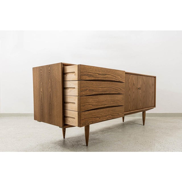 This Mid-Century Modern sideboard from Bydgoskie Fabryki Mebli in Poland, dating back to the 1960s, features a robust ash-...