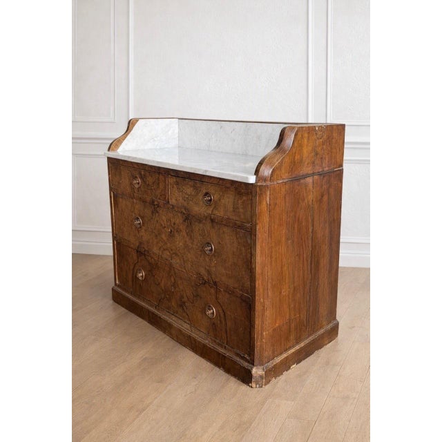 A walnut chest of drawers with a marble top, likely French-made, dating back to the early 1900s. This antique chest of...