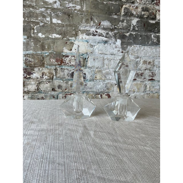 A stunning pair of vintage cut crystal perfume bottles with faceted geometric stoppers—one sharp and angular, the other...