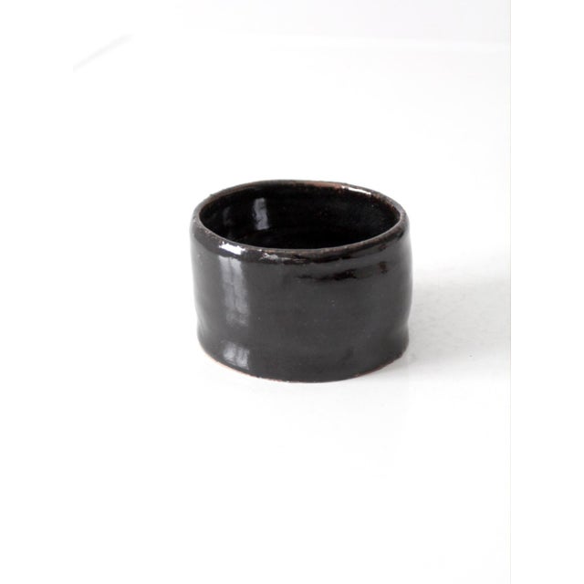 Vintage handmade studio pottery bowl with a low rounded form and glossy dark brown glaze that deepens to nearly black. Its...