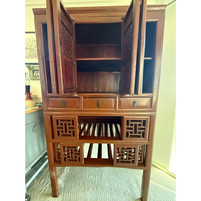 A large two-part wooden storage cabinet featuring four upper panel doors with intricately carved openwork fretwork...
