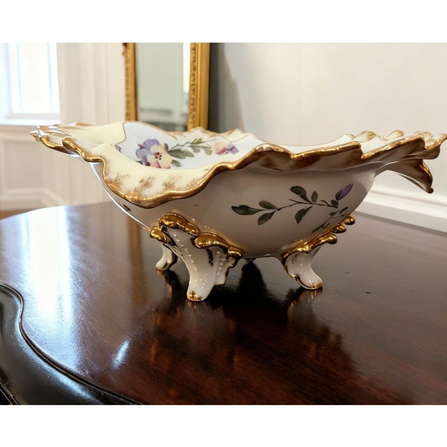 Elegant vintage porcelain centerpiece bowl featuring a dramatic scalloped silhouette, ornate raised shell-form feet, and...