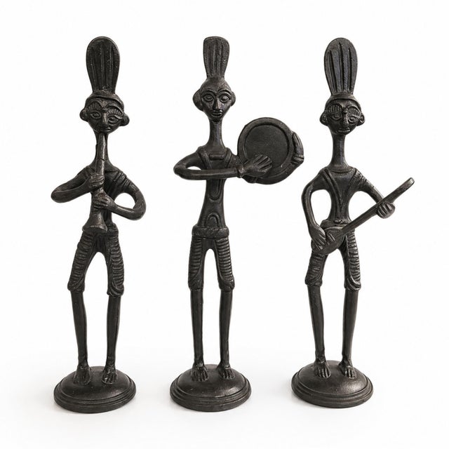 Striking set of three vintage cast iron musician figurines featuring elongated African tribal-inspired forms. Each figure...