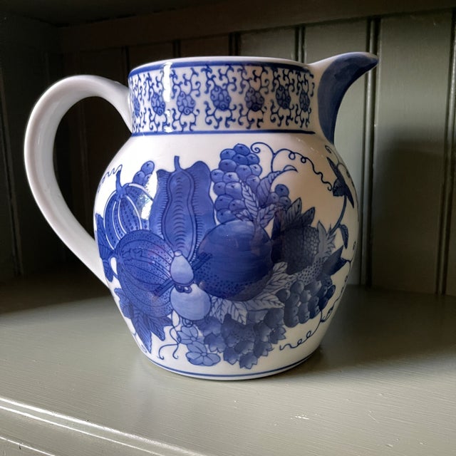 Lovely blue and white glazed ceramic pitcher. Grapes and vines, gourds, and flowers are hand painted in blue on a white...