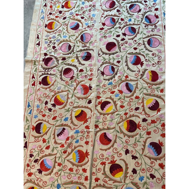Hand-embroidered Suzani panel from Uzbekistan — multicoloured pomegranate buds in plum, rose and gold scattered across an...
