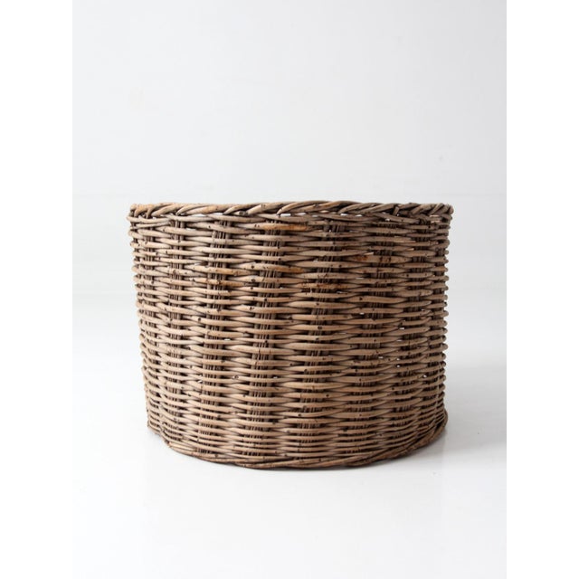 A large antique woven basket in a warm, natural tone with a grounded, organic presence. Its rounded form and subtle...