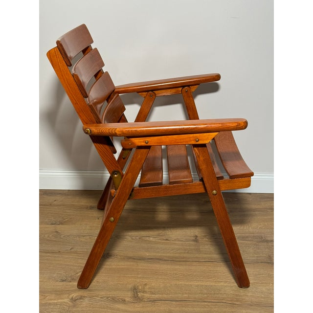 Folding garden chair “Capri” by Jung, crafted from solid lacquered wood in a warm honey tone. This piece has an...