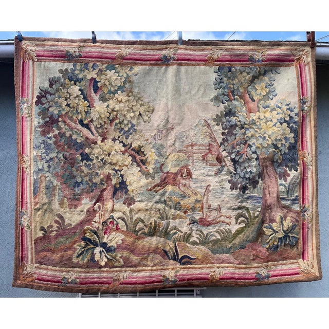 Charming 19th-century French tapestry depicting a pastoral landscape with a playful hunting scene. At the center of the...