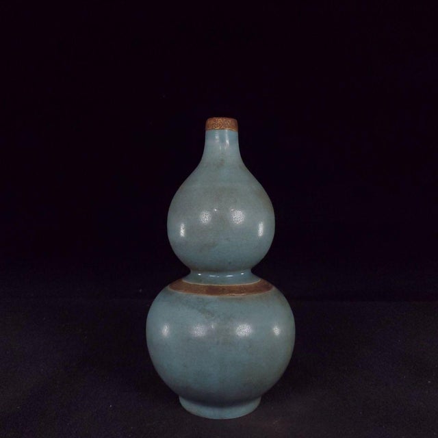 This elegant double-gourd shaped vase features soft sky-blue Ru-style celadon glaze with subtle crackle texture. Metal...