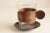 Set of 7 glass cups with patterned copper wrap and saucers signed "Schaefer Handarbeit". This item includes restricted...
