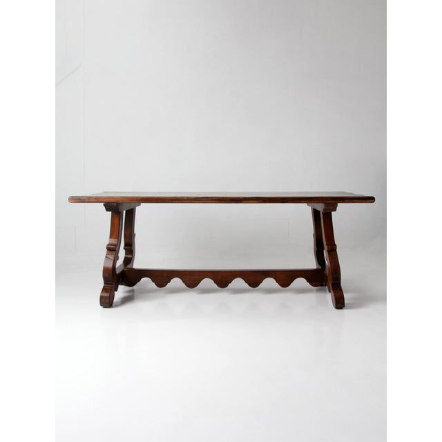 A substantial trestle table with a solid wood top and a carved base defined by shaped supports and a scalloped stretcher....