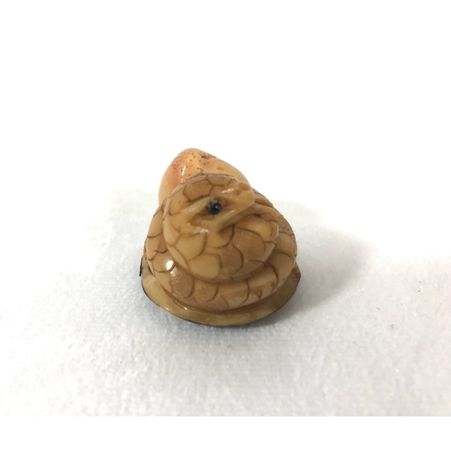 A netsuke style coiled auspicious snake resting on a platform with a symbolic long life peach, very intricately hand...