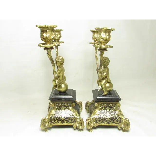 Pair of Italian figural bronze putti candlesticks, c.1880 Each putti holding up a candelabra arm and seated on a ball. The...