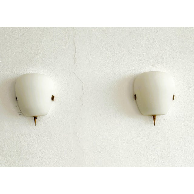 Minimalistic pair of french wall lights, made of milky white glasses. The glasses are held in place by a minimalist brass...