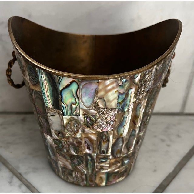 A solid brass ice bucket with tongs from Taxco, Mexico, covered in abalone shell tile overlay. Marked made in Mexico on...