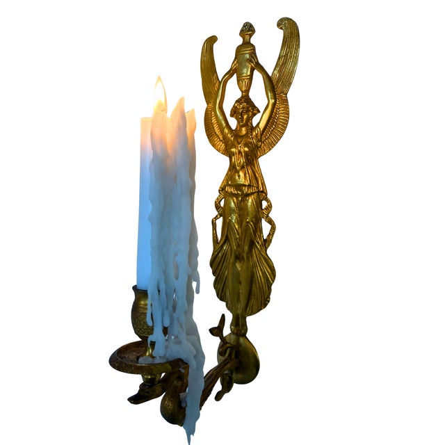 A striking French wall sconce in solid gilded bronze, depicting a finely sculpted winged Isis figure holding a sacred urn...