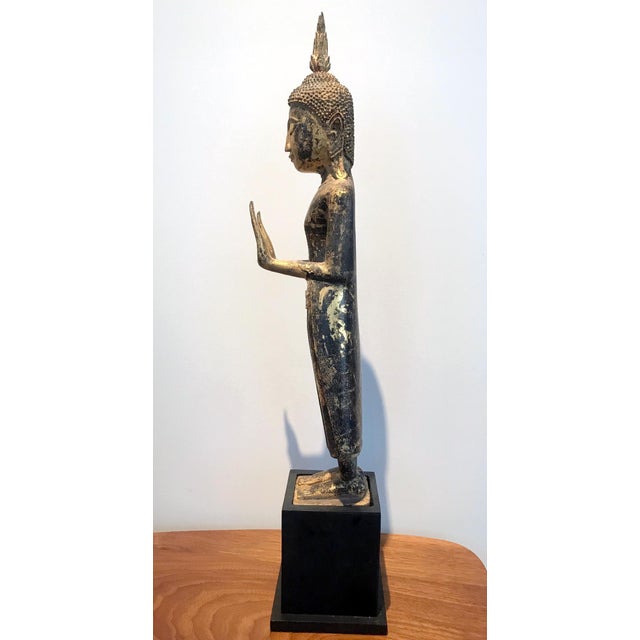 A delicately carved wood Buddha in an upright standing posture with a double Abhaya mudra. The statue displays a gilt...