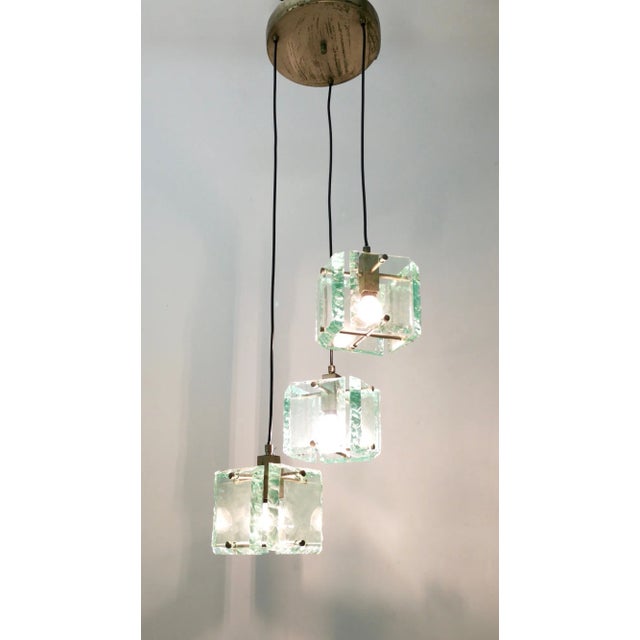 Made in Italy, 1960s. This pendant features thick Nile green hammered glass lampshades and varnished metal parts. The...