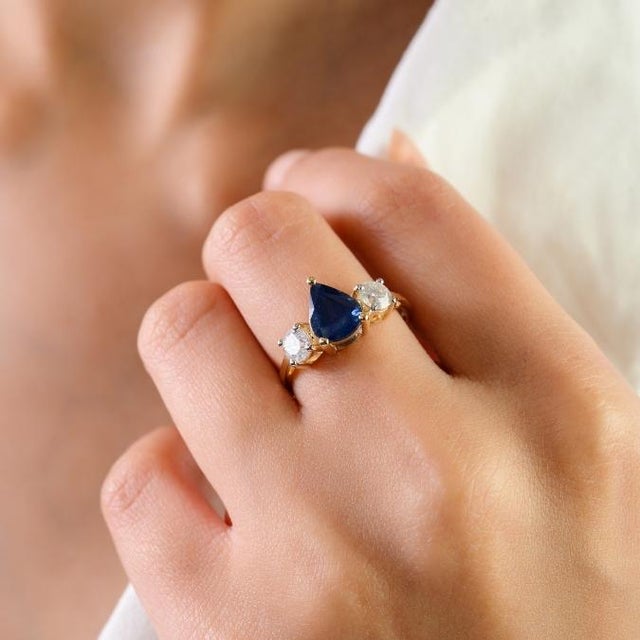 This elegant three-stone ring features 1 natural pear-cut blue sapphire totaling 1.7 carats, set ing rich 14k yellow gold....