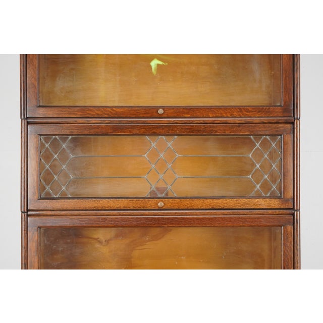 Antique four section oak wood barrister bookcase. It features original brass knobs and one etched glass door front. Made...