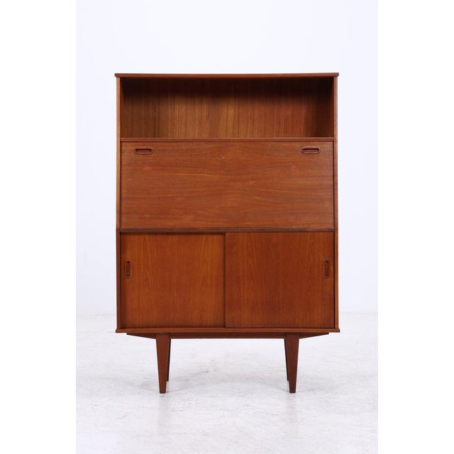 Vintage teak cabinet with an integrated writing flap and a well-organized interior. Behind the flap are several shelves,...