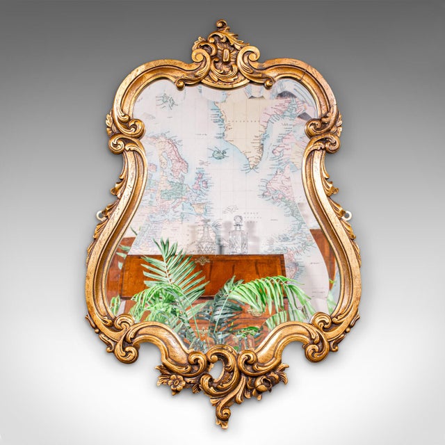 This is an antique Baroque wall mirror. A French, ornate giltwood vanity mirror, dating to the Edwardian period, circa...