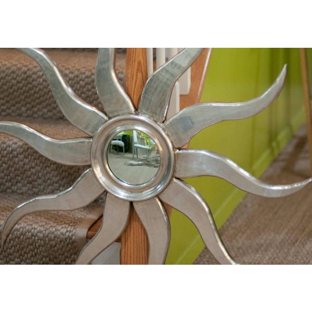 A whimsical, sunburst mirror in silvered wood with wavy rays and a molded centre.