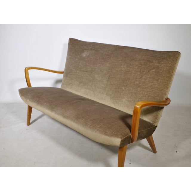 Vintage cocktail sofa with a velour cover from the 1960s. The curved wooden armrests, tapered legs, and softly padded seat...