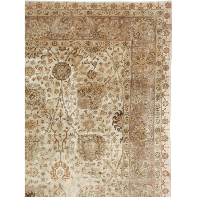 This mid-20th-century Persian Tabriz carpet presents an elegant allover floral composition across a warm ivory field....