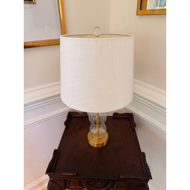 Contemporary Jonathan Y table lamp featuring a stacked clear glass globe and base with brushed brass-finish metal accents...
