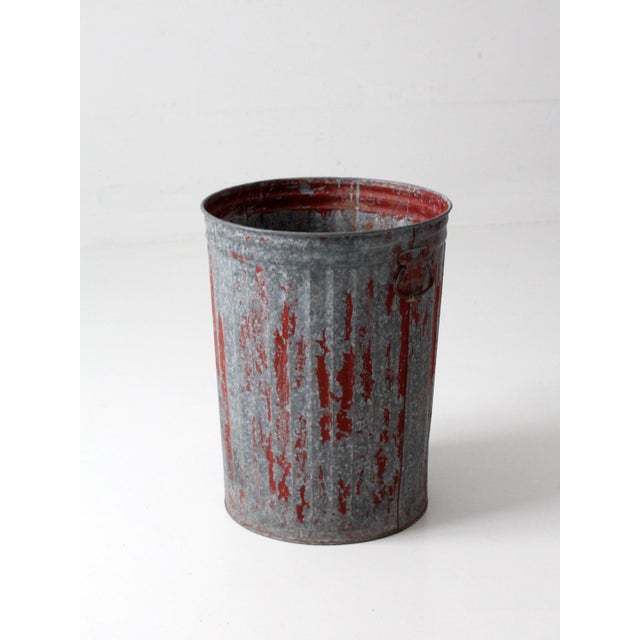 Early 20th century utility can featuring layers of weathered red paint over galvanized steel, creating a richly textured...