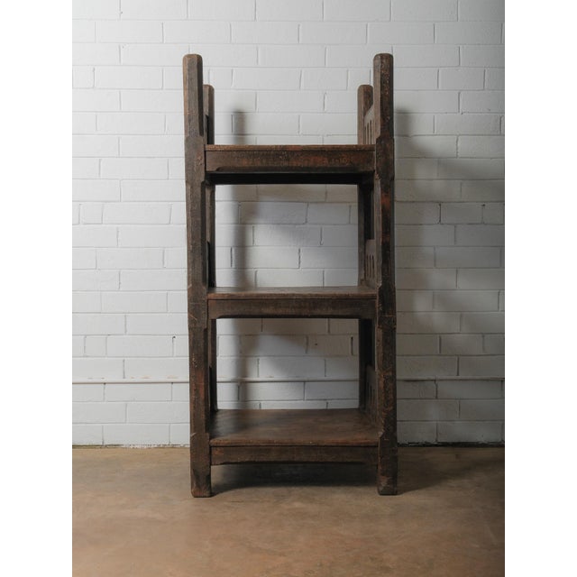 A striking wooden shelf unit defined by its sculptural, architectural presence. The frame is constructed with thick,...